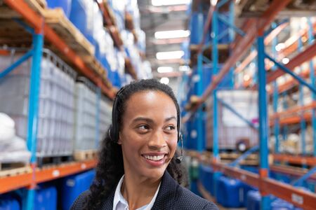 Close-up of happy female manager talking on headset in warehouse. This is a freight transportation and distribution warehouse. Industrial and industrial workers conceptの写真素材