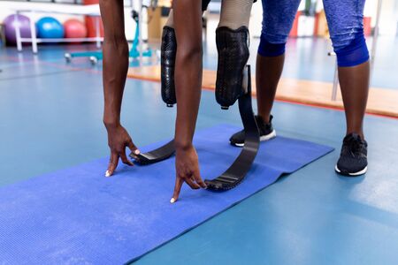 Low section of African-american female trainer assisting disabled African-american man while exercising in sports center. Sports Rehab Centre with physiotherapists and patients working together towards healingの写真素材