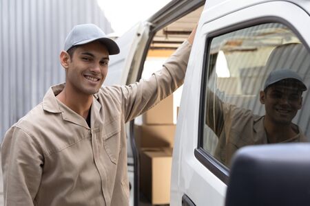 Front view of delivery man standing near van outside the warehouse. This is a freight transportation...