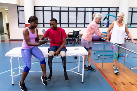 Front view of African-american female trainer helping and discussing with diverse disabled man and...