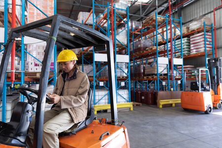 Front view of female worker using digital tablet while sitting in forklift in warehouse. This is a...