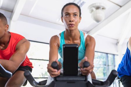 Close-up of African-american fit woman exercising on exercise bike in fitness center. Bright modern...