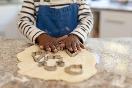 Front view mid section of a young mixed race boy in a kitchen at Christmas, making cookies and...