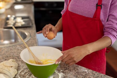 Side view mid section of a mixed race woman in a kitchen at Christmas, making cookies, cracking an...