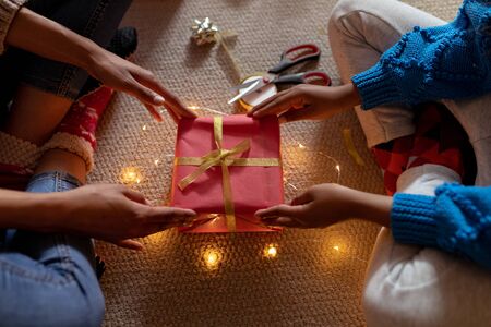 Front view mid section of a mixed race woman sitting on the floor with her young daughter in their sitting room at Christmas, holding a presentの写真素材