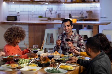 Front view of a group of young adult multi-ethnic male and female friends sitting around a table...