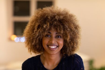 Portrait of a happy young mixed race woman with curly hair smiling to camera at home at night