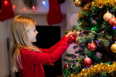 Side view of a young Caucasian girl decorating the Christmas tree in the sitting room at Christmas timeの写真素材