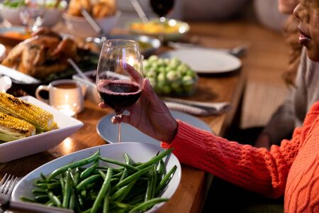 Side view of a young mixed race woman sitting at a table at home set for Thanksgiving dinner holding...