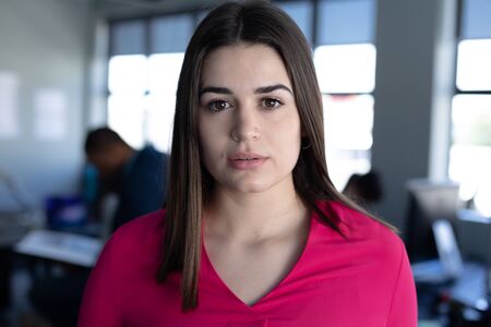 Portrait close up of a Caucasian female business creative with shoulder length dark hair working in a casual modern office, standing and looking straight to cameraの写真素材