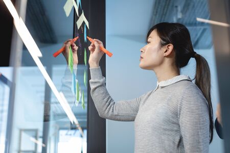 Side view of an Asian female business creative working in a casual modern office, standing and...