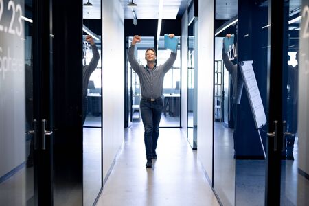 Front view of a Caucasian male business creative walking in the corridor of a modern office, raising...