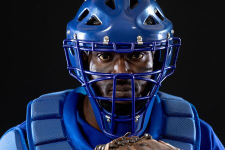 Portrait close up of an African American male baseball player, a catcher, wearing a team uniform,...