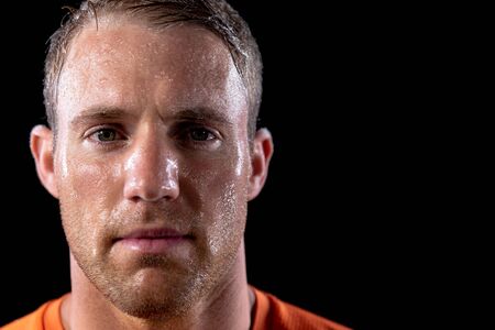 Portrait close up of a Caucasian male athlete sweating after a work out, looking straight to camera. On black backgroundの写真素材