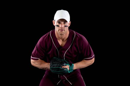 Front view of a Caucasian male baseball player, a fielder, wearing a team uniform, baseball cap and a mitt, waiting for a hit to catch, with stripes of eye black under his eyesの写真素材