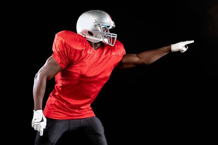 Side view of an African American male American football player wearing a team uniform, pads and a helmet pointing his fingerの写真素材