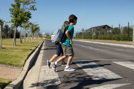 Side view of two Caucasian schoolboys crossing the road on a pedestrian crossing on their way to elementary school on a sunny dayの写真素材