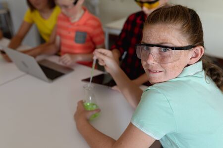 Side view close up of a Caucasian girl wearing safety glasses and a green t shirt, sitting at a desk...