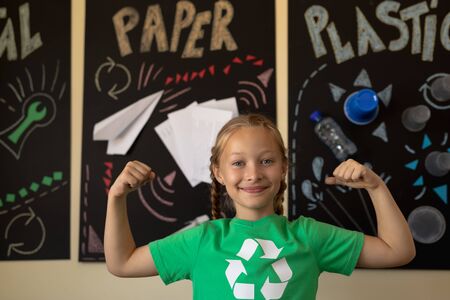 Portrait of a Caucasian schoolgirl with plaits wearing a green t shirt with a white recycling logo...