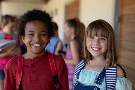 Front view close up of an African American schoolboy and a Caucasian schoolgirl standing together in...