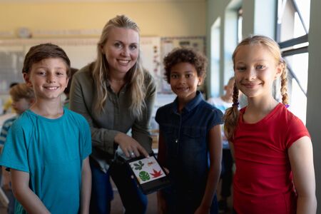 Portrait of a Caucasian female elementary school teacher with long blonde hair and a diverse group...