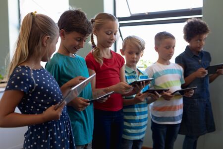 Side view of a diverse group of schoolchildren standing in a line all using tablet computers in an elementary school classroomの写真素材