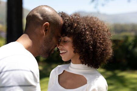 Side view close up of a mixed race couple standing in the garden, embracing, touching heads and...