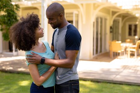 Side view of a mixed race couple standing in the garden outside their house, embracing and smiling...