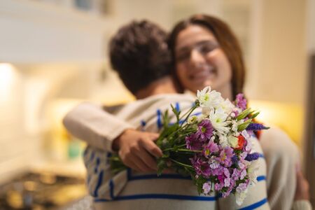 Rear view of a Caucasian couple at home embracing, the man giving the woman a bunch of flowers, the woman smilingの写真素材