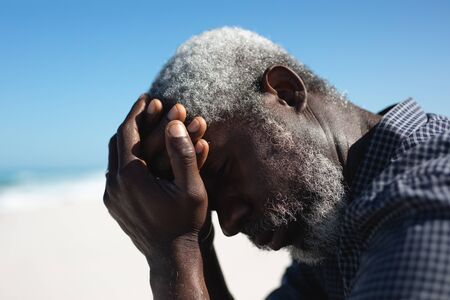 Side view close up of a senior African American man sitting on the beach with blue sky in the...