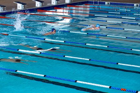 High angle side view of multi-ethnic group of male swimmers at swimming pool, racing each other in...