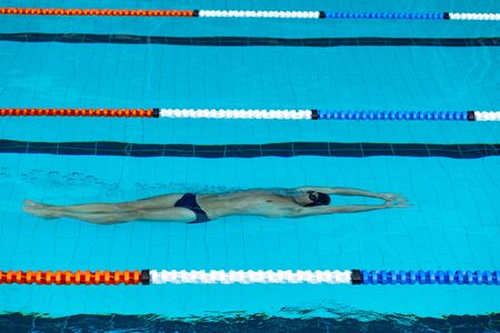 High angle side view of Caucasian male swimmer at swimming pool, swimming under water on his back,...