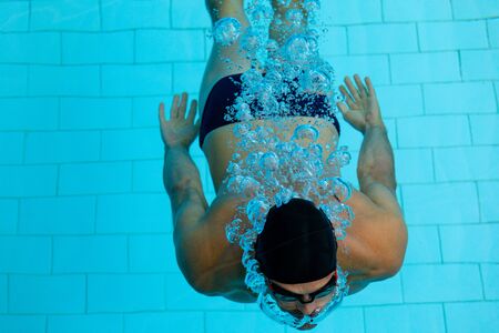 High angle front view of Caucasian male swimmer at swimming pool, , submerged in water, wearing black swimming cap and swimming gogglesの写真素材
