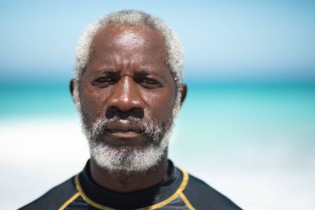 Portrait of a senior African American man on a beach in the sun, looking straight to camera, with blue sky and sea in the backgroundの写真素材