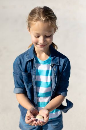 Front view close up of a Caucasian girl on a sunny beach, holding a seashell in her cupped hands, looking down at it and smilingの写真素材