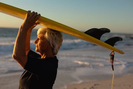 Side view close up of a senior Caucasian woman at the beach at sunset, standing on the sand holding...