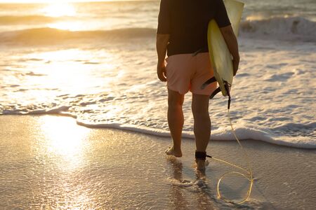 Low section rear view of a senior Caucasian woman at the beach at sunset, walking on the sand...