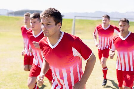 Front view close up of a group of Caucasian male football players wearing their team strip, training at a sports field, running together on a grass trackの写真素材