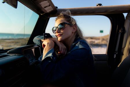 Front view of a Caucasian woman inside an open top car, holding a steering wheel and looking away....