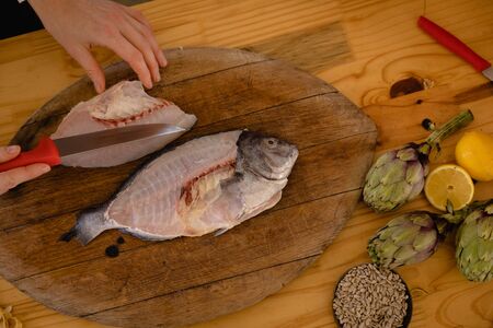 High angle view of a fish on a wooden chopping board, ready for preparation, on a wooden table in a...