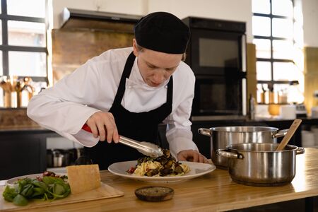 Front view of a Caucasian woman at a cookery class, adding ingredients to a fresh cooked pasta. Active Seniors enjoying their retirement.の写真素材