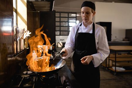 Front view of a Caucasian woman at a cookery class, frying vegetables on a frying pan, flaming....