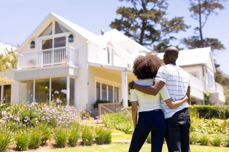 Weekend fun at home together. Rear view of a mixed race couple standing in the garden, embracing and looking at the houseの写真素材