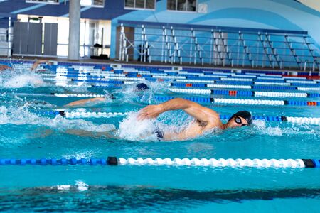 Side view of multi-ethnic group of male swimmers at swimming pool, racing each other in lanes, swimming crawl. Swimmers training hard for competition.の写真素材