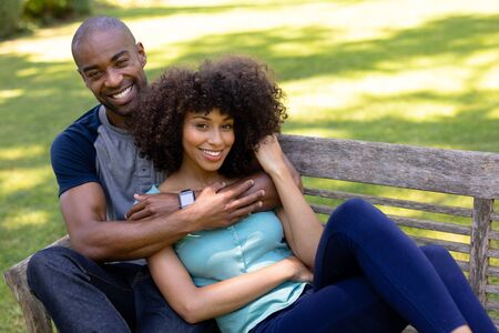 Weekend at home together. Front view of a mixed race couple sitting on a bench in the garden,...