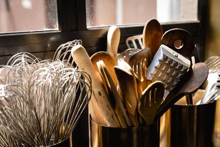 Close up of kitchen untensils standing in pots, sitting in front of a window in the sun, in a restaurant kitchenの写真素材