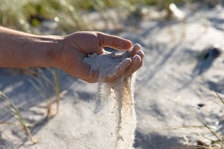 Mid section close up of a Caucasian man on the beach, pouring sand during a sunny day