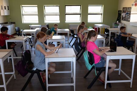 Side view of a diverse group of schoolchildren concentrated sitting at desks