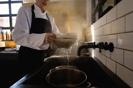 Side view of a Caucasian female chef at a cookery class in a restaurant kitchen, sieving freshly...
