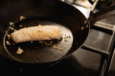 High angle view of a fillet of fish cooking in a frying pan on the hob, being prepared during a...